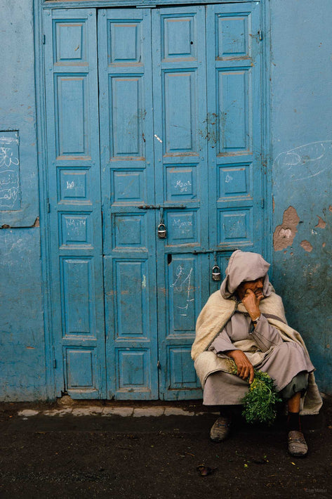 Man Holding Greens Sitting Against Blue Paneled Door, Marrakech