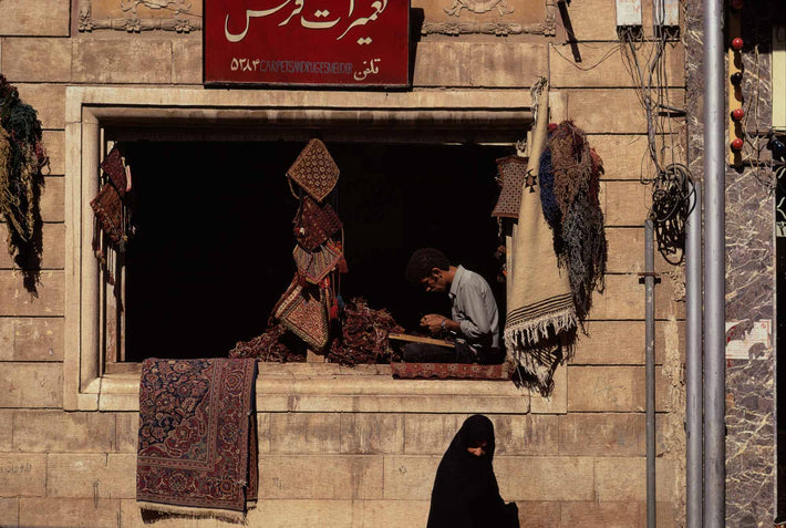 Man Sitting in Rug Store Window, Woman Walking By, Iran